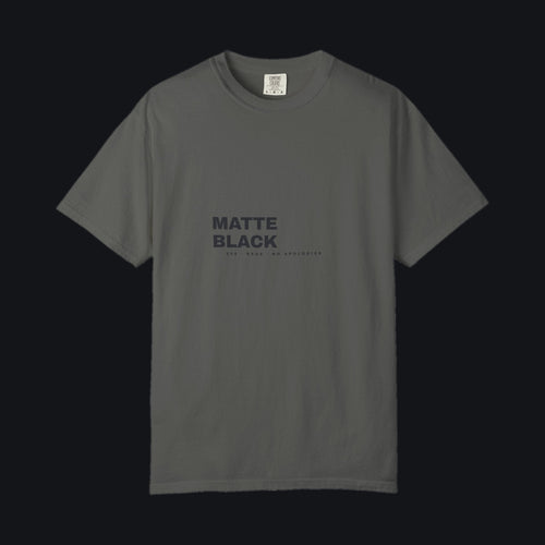 Matte Black Tee — Comfort Colors Pepper, tonal MATTE BLACK chest print, shown on the Jacob Day studio ground
